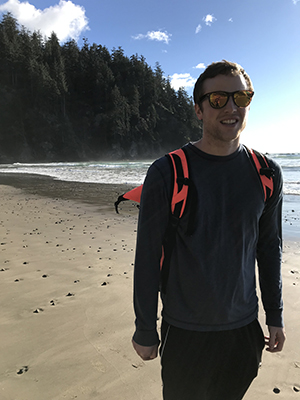 A man standing on a beach smiling wearing sunglasses.
