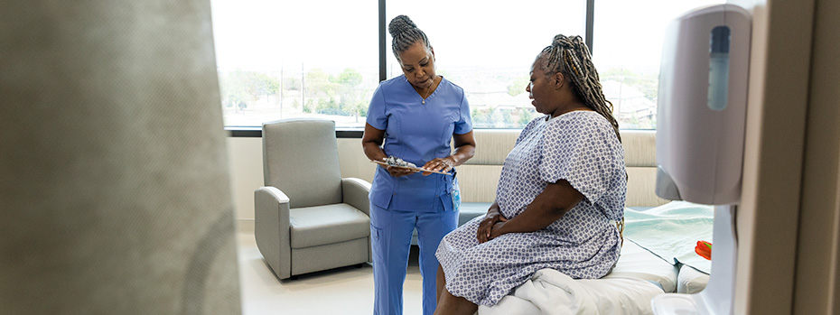An OHSU nursing student wearing scrubs reviews information on a tablet with a patient in a clinical setting.