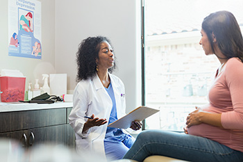 An OHSU nurse-midwifery student holding a clipboard talks with a patient.